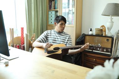 Güneydoğu Asyalı adam ilk defa internetten gitar çalmayı öğreniyor.