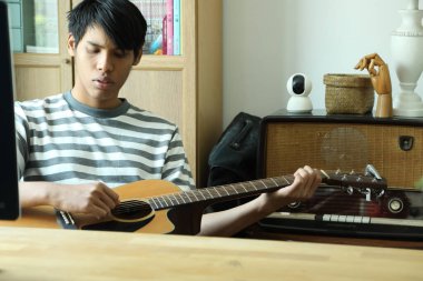 Güneydoğu Asyalı adam ilk defa internetten gitar çalmayı öğreniyor.