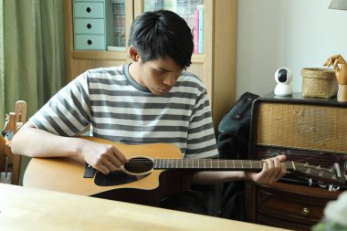 Güneydoğu Asyalı adam ilk defa internetten gitar çalmayı öğreniyor.