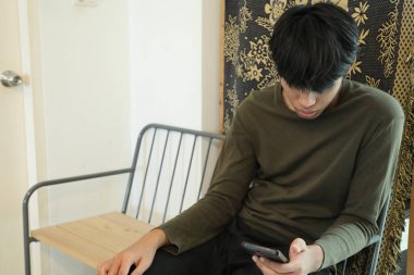 Güneydoğu Asyalı adam oturma odasında akıllı telefon kullanıyor..