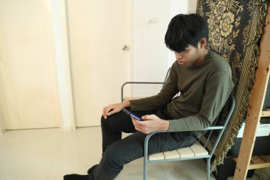 Güneydoğu Asyalı adam oturma odasında akıllı telefon kullanıyor..