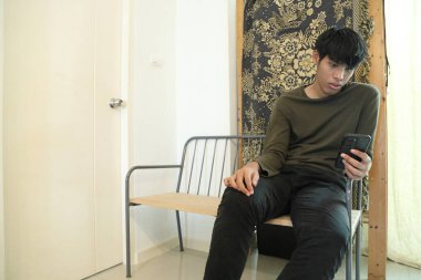 Güneydoğu Asyalı adam oturma odasında akıllı telefon kullanıyor..