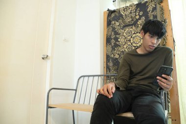 Güneydoğu Asyalı adam oturma odasında akıllı telefon kullanıyor..