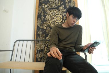 Güneydoğu Asyalı adam oturma odasında akıllı telefon kullanıyor..