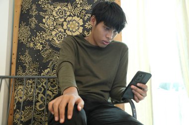 Güneydoğu Asyalı adam oturma odasında akıllı telefon kullanıyor..