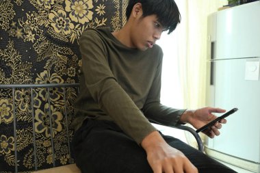 Güneydoğu Asyalı adam oturma odasında akıllı telefon kullanıyor..