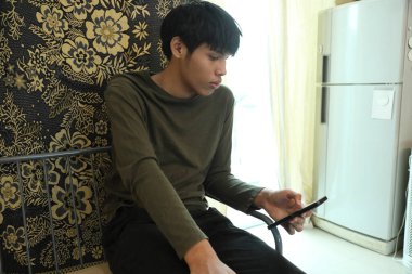 Güneydoğu Asyalı adam oturma odasında akıllı telefon kullanıyor..