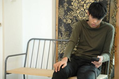 Güneydoğu Asyalı adam oturma odasında akıllı telefon kullanıyor..