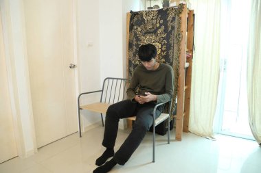 Güneydoğu Asyalı adam oturma odasında akıllı telefon kullanıyor..