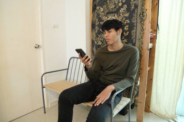 Güneydoğu Asyalı adam oturma odasında akıllı telefon kullanıyor..