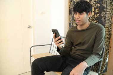 Güneydoğu Asyalı adam oturma odasında akıllı telefon kullanıyor..