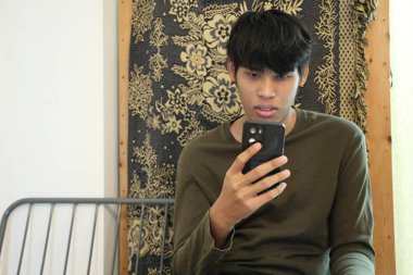 Güneydoğu Asyalı adam oturma odasında akıllı telefon kullanıyor..