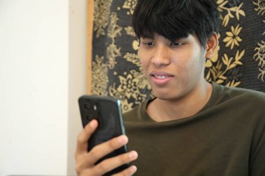 Güneydoğu Asyalı adam oturma odasında akıllı telefon kullanıyor..