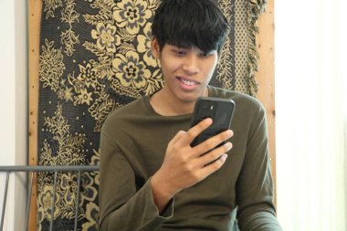 Güneydoğu Asyalı adam oturma odasında akıllı telefon kullanıyor..