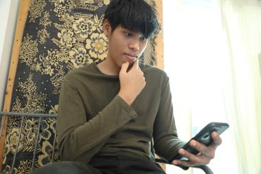 Güneydoğu Asyalı adam oturma odasında akıllı telefon kullanıyor..