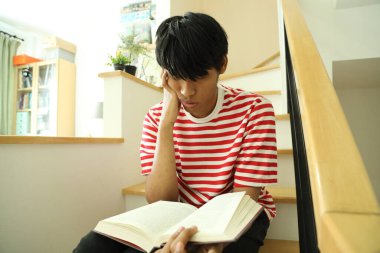 Güneydoğu Asyalı adam merdivenlerde kitap okuyor..