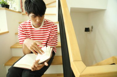 Güneydoğu Asyalı adam merdivenlerde kitap okuyor..