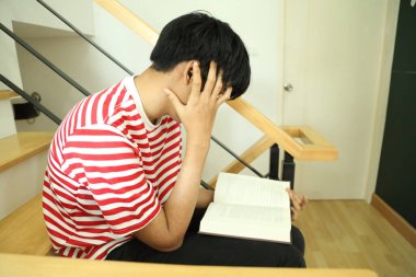 Güneydoğu Asyalı adam merdivenlerde kitap okuyor..