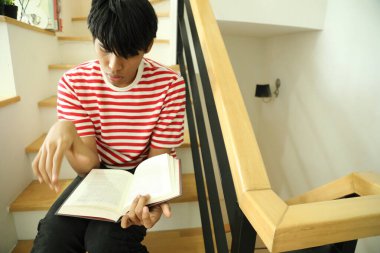 Güneydoğu Asyalı adam merdivenlerde kitap okuyor..