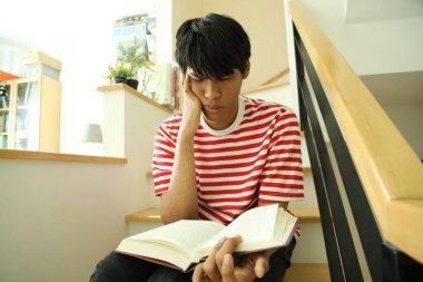 Güneydoğu Asyalı adam merdivenlerde kitap okuyor..