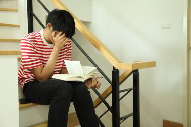 Güneydoğu Asyalı adam merdivenlerde kitap okuyor..