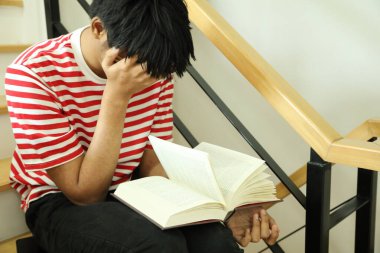 Güneydoğu Asyalı adam merdivenlerde kitap okuyor..