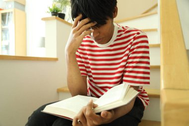 Güneydoğu Asyalı adam merdivenlerde kitap okuyor..