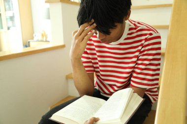 Güneydoğu Asyalı adam merdivenlerde kitap okuyor..