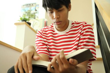 Güneydoğu Asyalı adam merdivenlerde kitap okuyor..