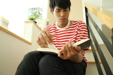 Güneydoğu Asyalı adam merdivenlerde kitap okuyor..