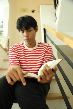 Güneydoğu Asyalı adam merdivenlerde kitap okuyor..