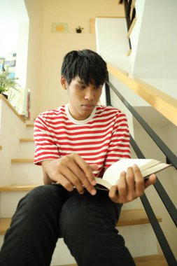 Güneydoğu Asyalı adam merdivenlerde kitap okuyor..
