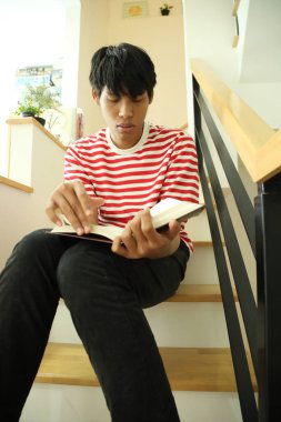 Güneydoğu Asyalı adam merdivenlerde kitap okuyor..