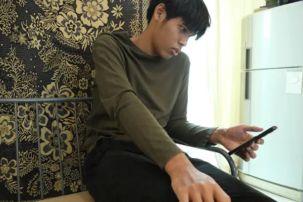 Güneydoğu Asyalı adam oturma odasında akıllı telefon kullanıyor..