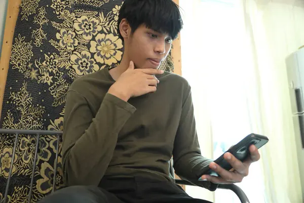 Güneydoğu Asyalı adam oturma odasında akıllı telefon kullanıyor..