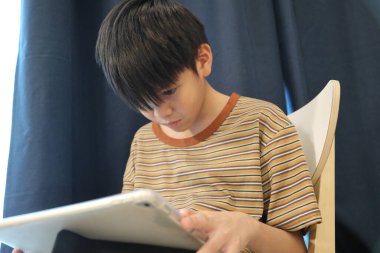 Güneydoğu Asyalı çocuk oturma odasında dijital tablet kullanıyor..