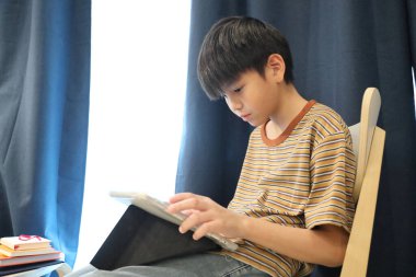 Güneydoğu Asyalı çocuk oturma odasında dijital tablet kullanıyor..