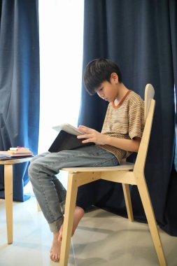 Güneydoğu Asyalı çocuk oturma odasında dijital tablet kullanıyor..