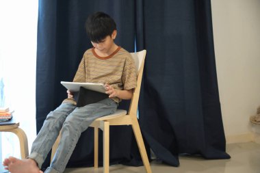 Güneydoğu Asyalı çocuk oturma odasında dijital tablet kullanıyor..