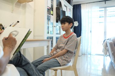 Güneydoğu Asya 'lı bekar anne oğlunun hareketsiz otururken resmini çiziyor..