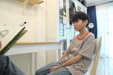 Güneydoğu Asya 'lı bekar anne oğlunun hareketsiz otururken resmini çiziyor..