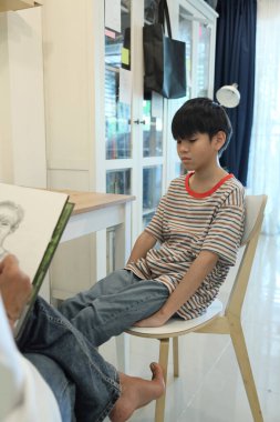 Güneydoğu Asya 'lı bekar anne oğlunun hareketsiz otururken resmini çiziyor..