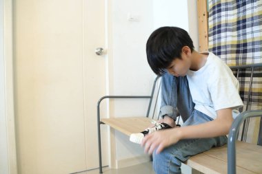 Güneydoğu Asyalı çocuk evden çıkmadan önce ayakkabılarını giyiyor..