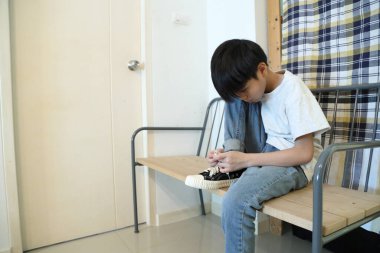 Güneydoğu Asyalı çocuk evden çıkmadan önce ayakkabılarını giyiyor..