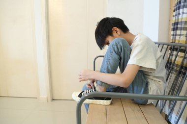 Güneydoğu Asyalı çocuk evden çıkmadan önce ayakkabılarını giyiyor..