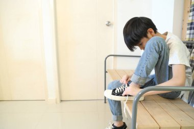 Güneydoğu Asyalı çocuk evden çıkmadan önce ayakkabılarını giyiyor..