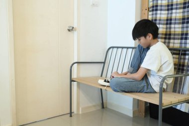 Güneydoğu Asyalı çocuk evden çıkmadan önce ayakkabılarını giyiyor..