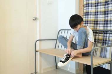 Güneydoğu Asyalı çocuk evden çıkmadan önce ayakkabılarını giyiyor..