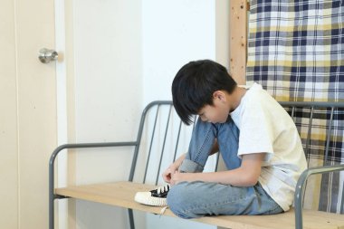 Güneydoğu Asyalı çocuk evden çıkmadan önce ayakkabılarını giyiyor..