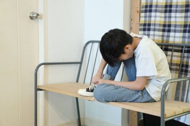 Güneydoğu Asyalı çocuk evden çıkmadan önce ayakkabılarını giyiyor..